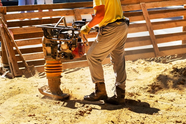 Chantier de construction extérieur avec ouvrier utilisant un compacteur pneumatique sur sol sablonneux