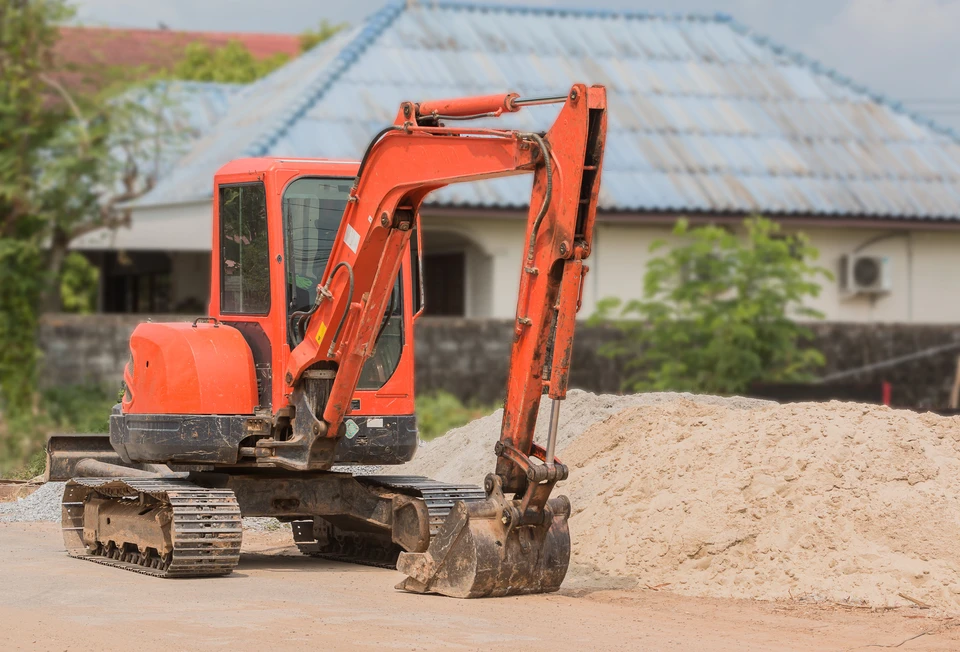 Chantier de construction extérieur avec une mini-pelle hydraulique orange stationnée près d'un tas de terre excavée