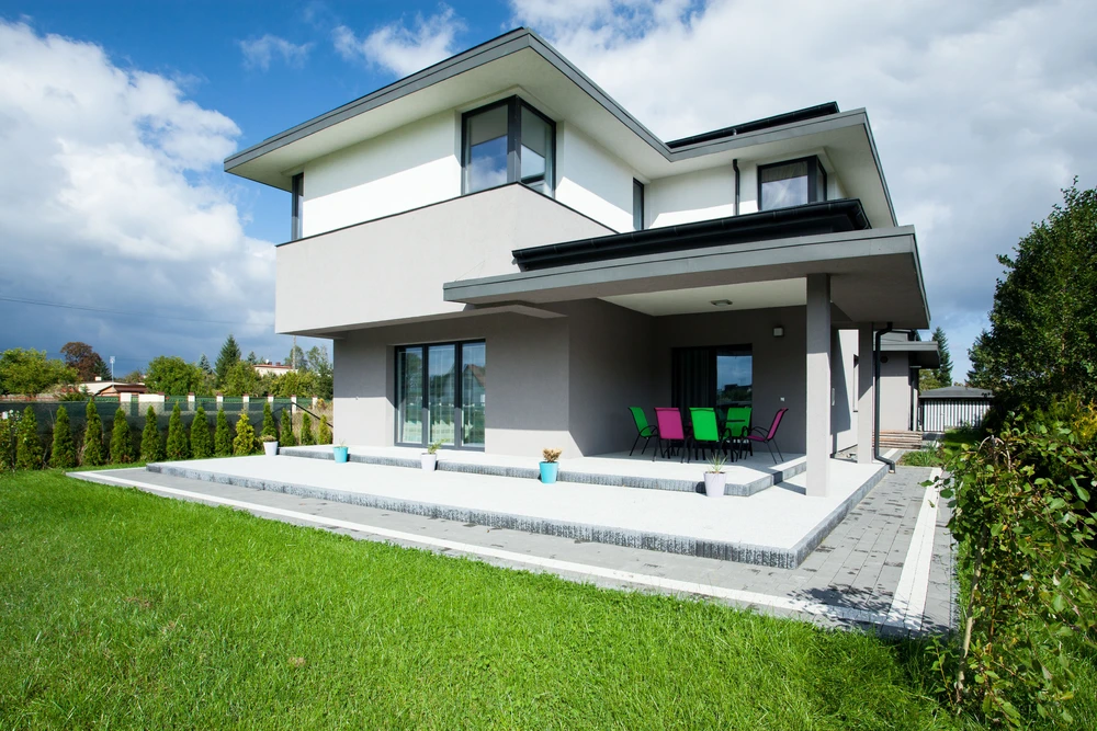 Maison contemporaine à deux niveaux avec terrasse couverte, mobilier coloré extérieur, pelouse entretenue et aménagement paysager