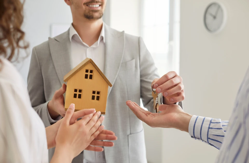 Trois ouvriers du bâtiment en casques de protection jaunes effectuent un geste de cohésion d'équipe, joignant leurs mains en l'air sur un chantier extérieur sous ciel bleu nuageux