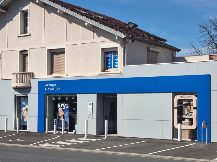 Bâtiment commercial moderne avec façade blanche et baies vitrées, situé dans une zone d'activité avec parking asphalté et éclairage public