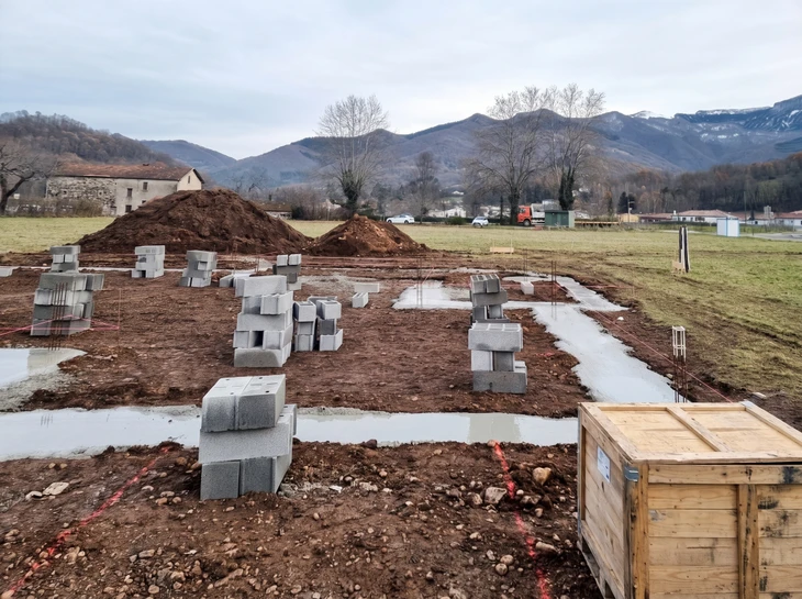 Chantier de construction résidentielle avec dalle béton fraîchement coulée au premier plan et maisons individuelles en briques en arrière-plan