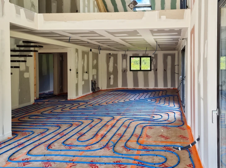 Intérieur résidentiel avec technicien en combinaison rouge et bleue installant un radiateur blanc à ailettes sur mur gris